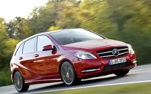 Czerwony Mercedes Klasy B w ruchu, z rozmytym tłem drzew i drogi.