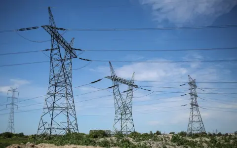Wysokie wieże energetyczne z przewodami na tle błękitnego nieba z chmurami.