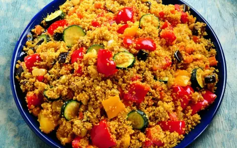 Un piatto colorato di cous cous con verdure miste: peperoni rossi e gialli, zucchine e melanzane.