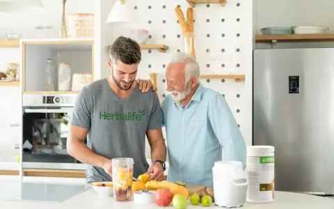 Två män i ett kök förbereder en smoothie med frukt. En burk med vegetariskt protein står på bänken.
