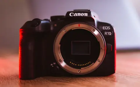 Canon EOS R10 w teście. Ciemna obudowa aparatu z czerwonym podświetleniem, widoczny bagnet obiektywu.