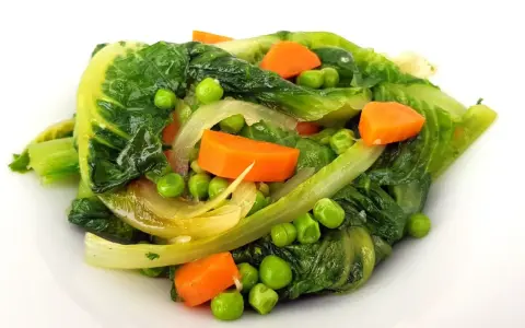 Un assortiment coloré de légumes verts feuillus, de pois et de carottes en dés, rappelant une jardinière de légumes fraîchement préparée.