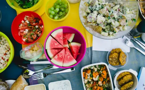 Bunte Schüssel mit Wassermelone, Kartoffelsalat, Trauben und Tomatensalat – leckere Picknick-Snacks für einen sonnigen Tag.