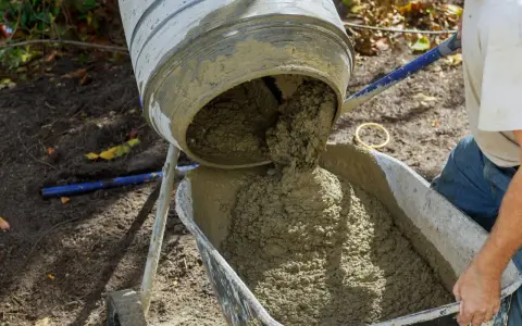 Beton B25 wylewa się z betoniarki do taczki. Proporcje na łopaty są kluczowe dla uzyskania odpowiedniej konsystencji.