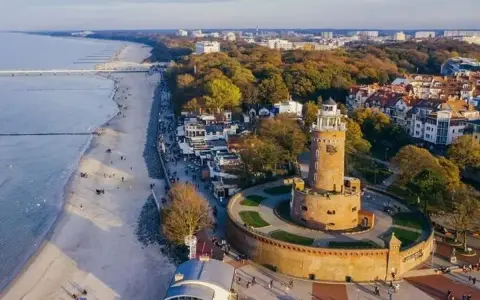 Widok z lotu ptaka na latarnię morską w Darłowie, plażę i nadmorskie miasteczko.