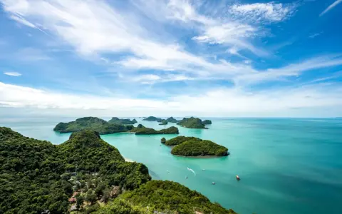Grüne Inseln ragen aus türkisfarbenem Wasser im Nationalpark Thailand. Kleine Boote gleiten über die ruhige See unter einem blauen Himmel mit weißen Wolken.