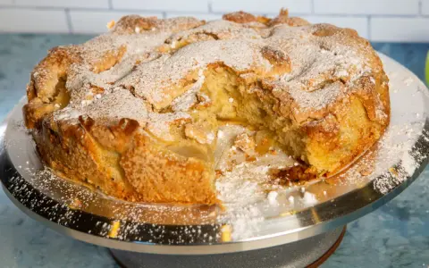 Pyszne, ekspresowe ciasto z jabłkami, posypane cukrem pudrem, prezentuje się apetycznie na srebrnej paterze.