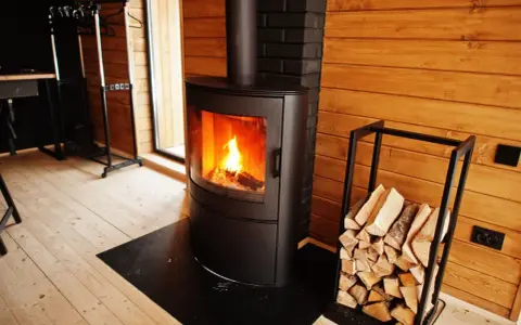 Estufas de leña canalizables modernas con fuego encendido y leña apilada, creando un ambiente acogedor en una cabaña de madera.