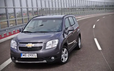 Szary Chevrolet Orlando 1.8 benzyna na pustej drodze, za barierami dźwiękochłonnymi.