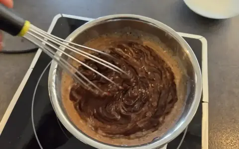 Préparation d'une recette ganache chocolat : du chocolat fondu est fouetté dans une casserole sur une plaque chauffante.