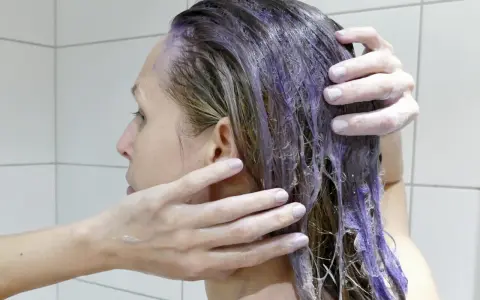 En person masserar in silverschampo med blå pigment i sitt blonda hår.