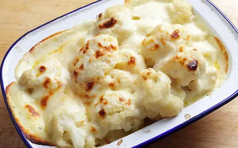 Coliflor gratinada con bechamel cremosa, dorada y burbujeante en una fuente.