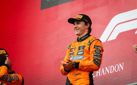 El piloto australiano F1, Oscar Piastri, sonríe en el podio con su mono naranja de McLaren.