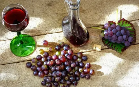 Szklanka z czerwonym winem, karafka z nalewką z winogron i świeże winogrona na drewnianym stole.