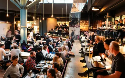 Folk äter och umgås på en livlig **Ringen food court**. Många bord är upptagna, stämningen är social och maten ser god ut.