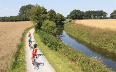 Radfahrer genießen die Fahrt auf dem werse ems radweg entlang eines Kanals und durch Felder.