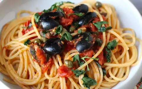 Un piatto invitante di spaghetti alla puttanesca, con olive nere, capperi e pomodoro fresco, guarnito con prezzemolo.