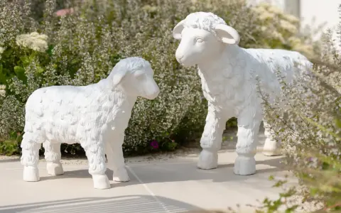 Deux adorables agneaux en résine, œuvres de sculpteurs animaliers, semblent converser au milieu d'une végétation luxuriante.