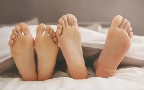 Piedi freddi in estate, nascosti sotto le lenzuola bianche. Due paia di piedi, uno più chiaro dell'altro, cercano calore.