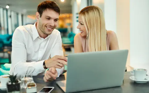Uśmiechnięci współpracownicy przy laptopie. Ich spojrzenia i gesty sugerują, że to nie tylko praca, ale i rodząca się miłość w pracy.
