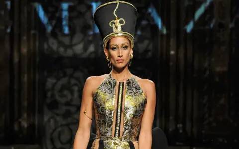 A model wears a striking Nefertiti-inspired headdress and ornate gold and black gown, showcasing the bold vision of Egyptian fashion designers.