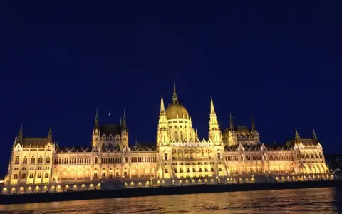 Budynek Parlamentu w Budapeszcie nocą, oświetlony, z odbiciem w Dunaju. Warto sprawdzić ceny na Węgrzech przed podróżą.