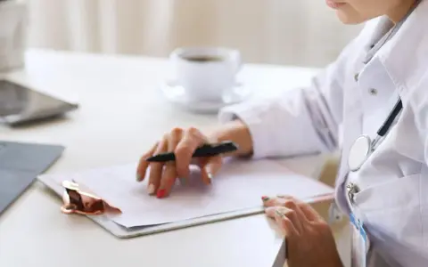 Médica revisa historial para tratamiento de hiperplasia endometrial. En su escritorio, laptop, tablet y café.