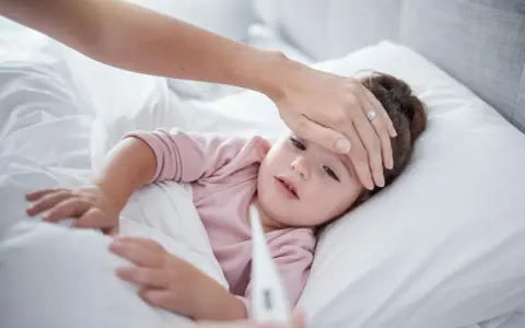 Mama sprawdza temperaturę chorego dziecka, martwiąc się przegrzaniem.