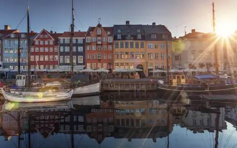 Färgglada hus vid en kanal i Köpenhamn, med båtar i förgrunden. Solen skiner och reflekteras i vattnet. En perfekt vy för en flyg till Köpenhamn-resa.