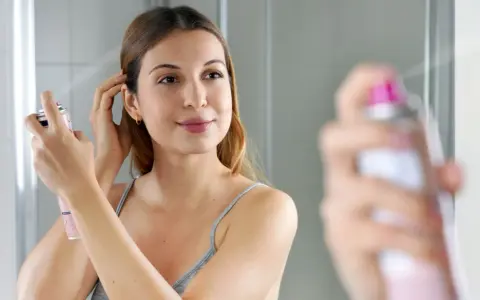 Frau sprüht sich Trockenshampoo ins Haar, um es aufzufrischen. So einfach ist es, wie man Trockenshampoo benutzt.