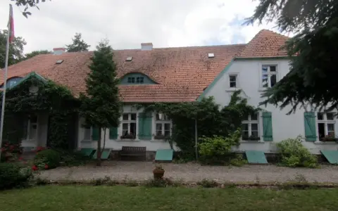 Dwór Wybickich otoczony zielenią, z charakterystycznym dachem i oknami.