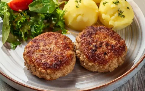 Dwa apetyczne kotlety mielone z airfryer, podane z ziemniakami i świeżą sałatką.