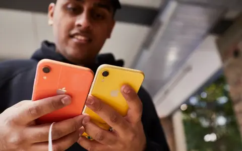 Mężczyzna trzyma dwa telefony: pomarańczowy i **iphone xr żółty**.