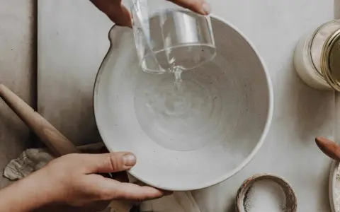 Wasser wird in eine Schüssel gegossen, vielleicht zu viel Wasser im Brotteig. Ein Nudelholz liegt daneben.