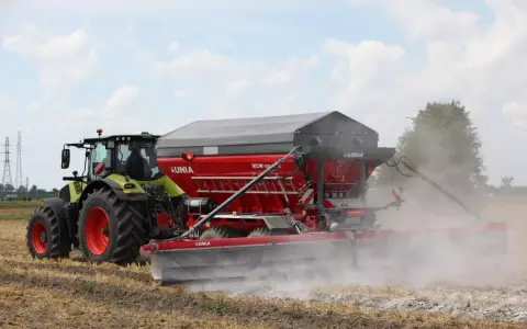 Traktor z rozsiewaczem wapna RCW 1300 marki UNIA na polu. To idealne rozwiązanie, jakie wapno pod warzywa, by zapewnić im najlepsze warunki do wzrostu.