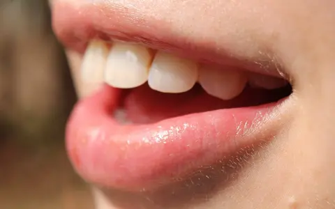 Uśmiech z białymi zębami, usta lekko rozchylone, jakby właśnie użyto nić dentystyczną do ich oczyszczenia.
