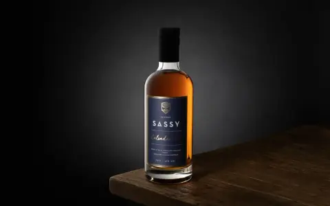 Packshot photo d'une bouteille de Calvados SASSY XO ambré, posée sur une table en bois.