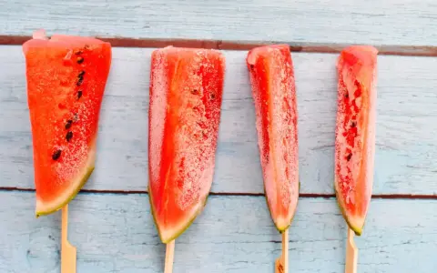 Vier gefrorene Wassermelonenstücke auf Stöcken, bereit zum Genießen. Eine erfrischende Idee für Wassermelone einfrieren.