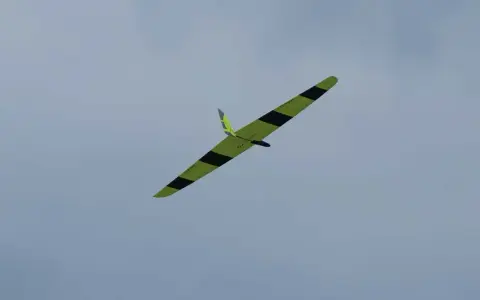 Ein gelb-schwarzes Flying Wing Segelflugzeug gleitet elegant durch den wolkenverhangenen Himmel.