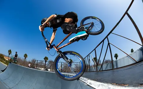 A BMX rider, possibly Chelsea Wolfe, performs a trick on a ramp against a clear blue sky.