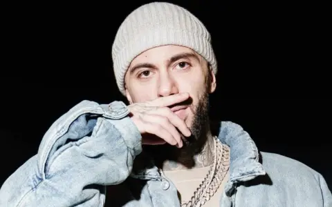 Malik Montana w czapce i jeansowej kurtce, z dłonią na ustach, gotowy na koncert.
