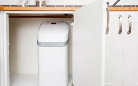 Un adoucisseur d'eau AEG blanc est installé sous un évier de cuisine. C'est une bonne idée de savoir quand installer un adoucisseur d'eau pour une eau plus douce.