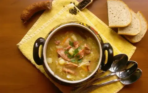 Aromaticzny kapuśniak jak u babci, z kiełbasą i ziemniakami, podany w ozdobnym garnku, obok kromek chleba i łyżek.