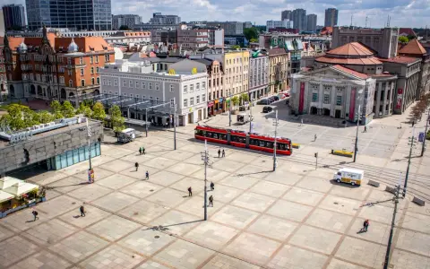 Rynek w Katowicach z czerwonym tramwajem i ludźmi spacerującymi po placu. Idealne miejsce na odkrywanie katowickich atrakcji dla młodzieży.