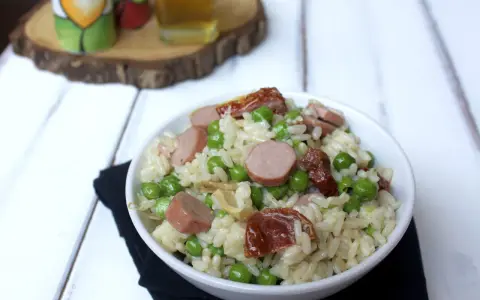 Una ciotola di insalata di riso con piselli, salsiccia e pomodori secchi, pronta per essere gustata.