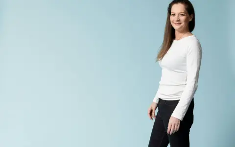 Kvinna i vit tröja och svarta jeans ler mot kameran, redo för en utmaning som fasta 24 timmar.
