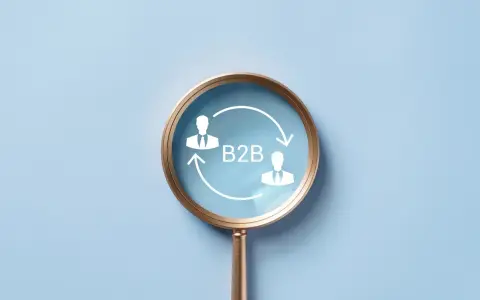 Lupa powiększa schemat B2B z dwoma ludzikami w garniturach i strzałkami, symbolizującymi współpracę biznesową.