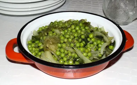 Un plat de petits pois et légumes verts, assaisonnés d'herbes, dans une cocotte orange. Une recette simple et savoureuse.