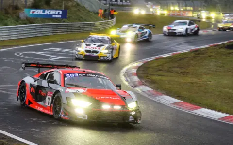 Un Audi R8 rojo y negro compite en las 24 Horas Nürburgring, con otros coches de carreras en la pista mojada.