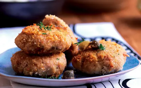Polpette tonno e patate dorate e croccanti, guarnite con erbe aromatiche e olive, pronte per essere gustate.